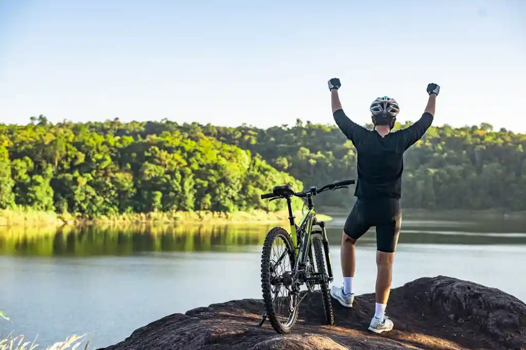 Homem de braços levantados com a bicicleta do lado ao ar livre