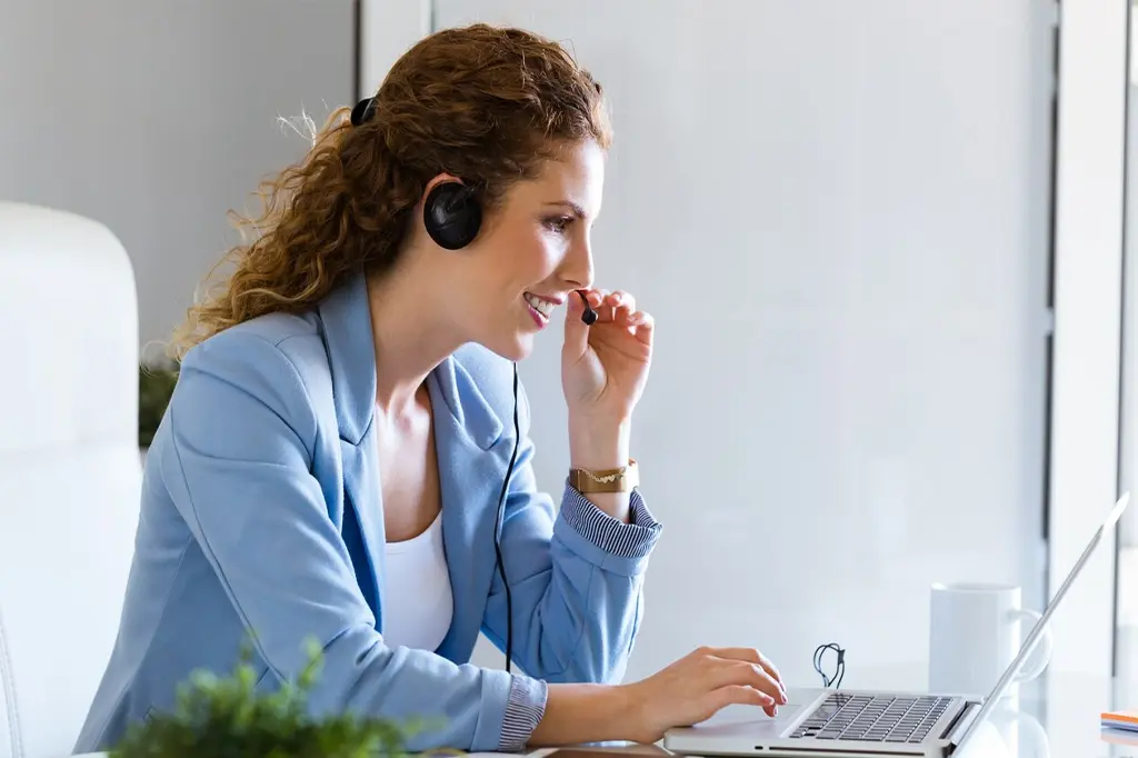 Mulher de telemarketing sorrindo e atendendo cliente por telefone.